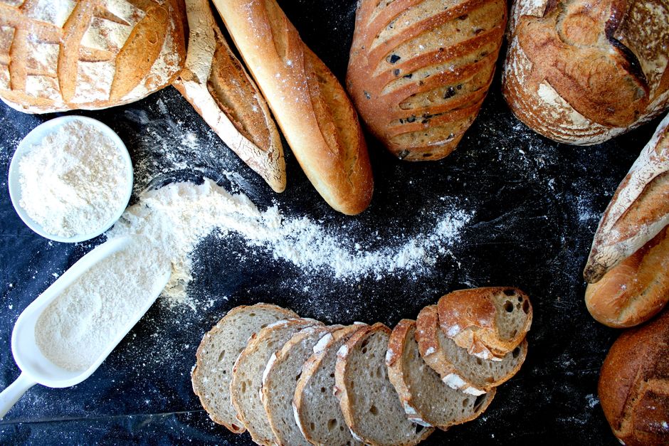 Brote, Baguettes und Mehl auf dunkler Arbeitsplatte