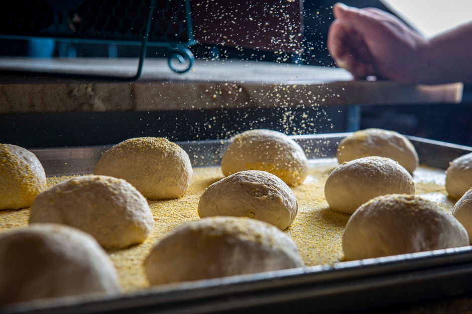 Teiglinge auf dem bemehlten Blech, eine Hand streut Mehl