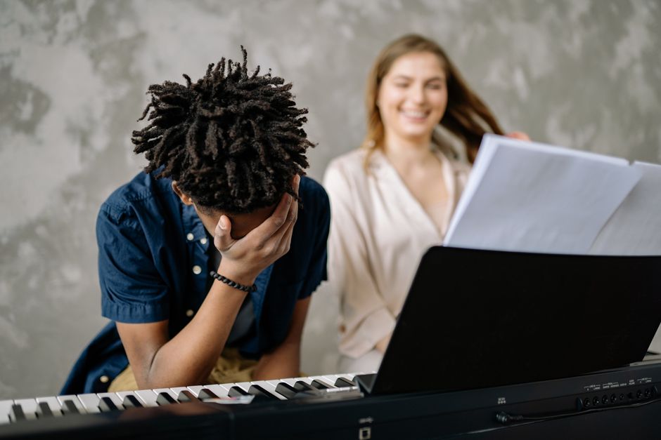 Schüler am Klavier fasst sich an den Kopf, die Lehrerin lacht aufmunternd